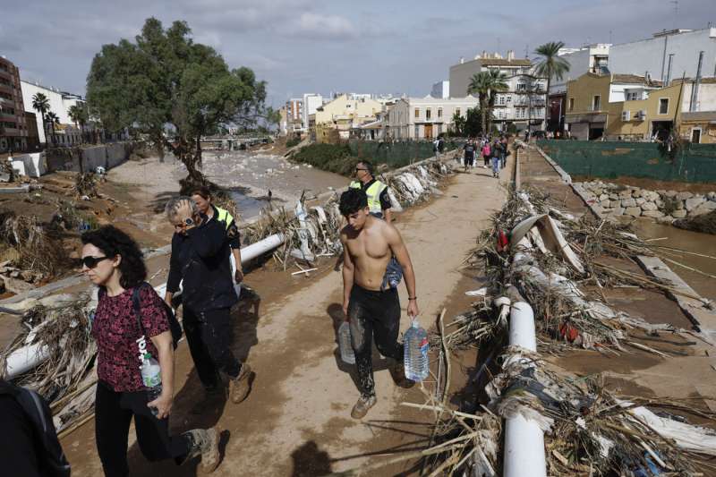 Varias personas transportan agua potable por uno de los puentes que cruza el barranco de Paiporta, Valencia, este jueves. La Comunitat Valenciana intenta recuperarse de la peor dana del siglo en Espaa, que ha dejado casi un centenar de muertos en esa regin, adems de un inmenso escenario de daos en carreteras, calles e infraestructuras de numerosas localidades. EFE Biel Alio