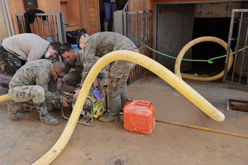 Soldados conectan una manguera a una bomba para ayudar a una vecina a achicar el agua del garaje en Paiporta. EFE Manuel BruqueArchivo