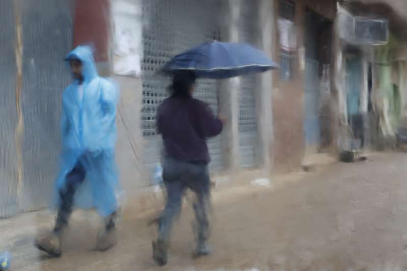 Fotografa tomada tras un cristal de dos personas que caminan protegida para la lluvia por Paiporta este mircoles.. EFEJorge Zapata
